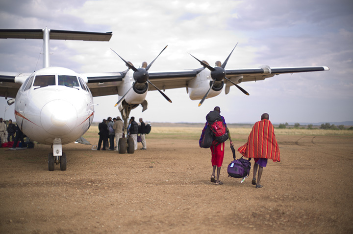 [image]ケニア、マサイマラの草原に降り立つ、荷物を運ぶマサイ族 ©藤巻 亮太